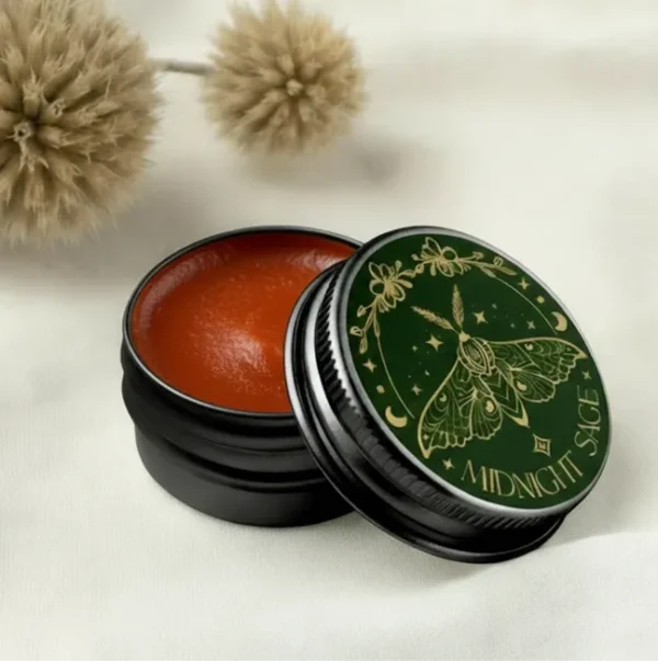 A tin of orange calendula salve resting on a cotton sheet, with tree seeds behind it.