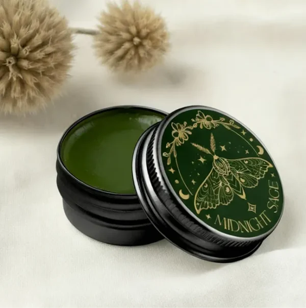 A tin of green comfrey salve resting on a cotton sheet, with tree seeds behind it.