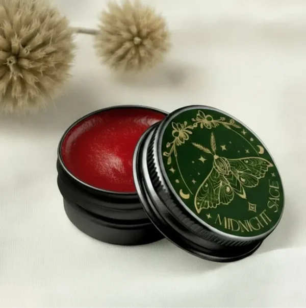 A tin of red St. John's wort salve resting on a cotton sheet, with tree seeds behind it.