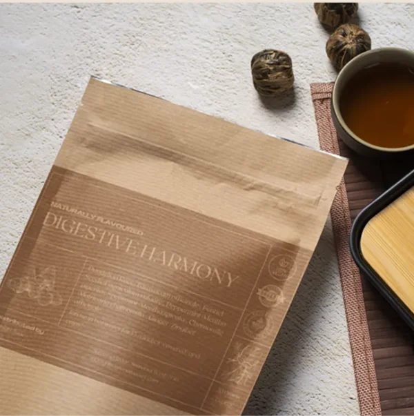 A bag of Digestive Harmony tea in a brown paper kraft bag lying on a table, next to a cup of freshly brewed tea and a bamboo cup rest.